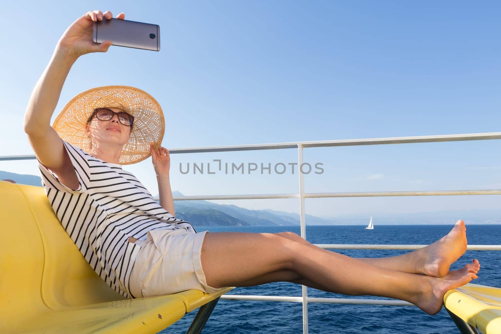 Beautiful, romantic blonde woman taking selfie self portrait on summer vacations traveling by cruse ship ferry boat. Summer vacation lifestyle.