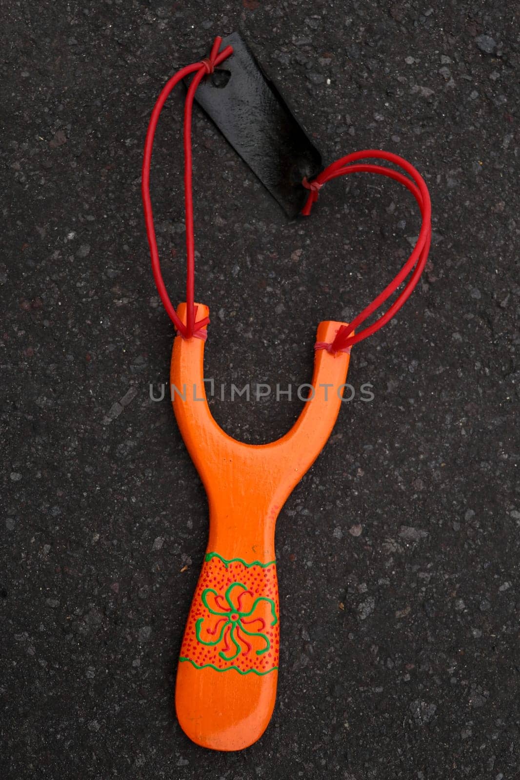 Handmade orange slingshot catapult. Y-shaped wooden stick with elastic tied between two top parts. Slingshot or Catapult is a device for shooting small stones.