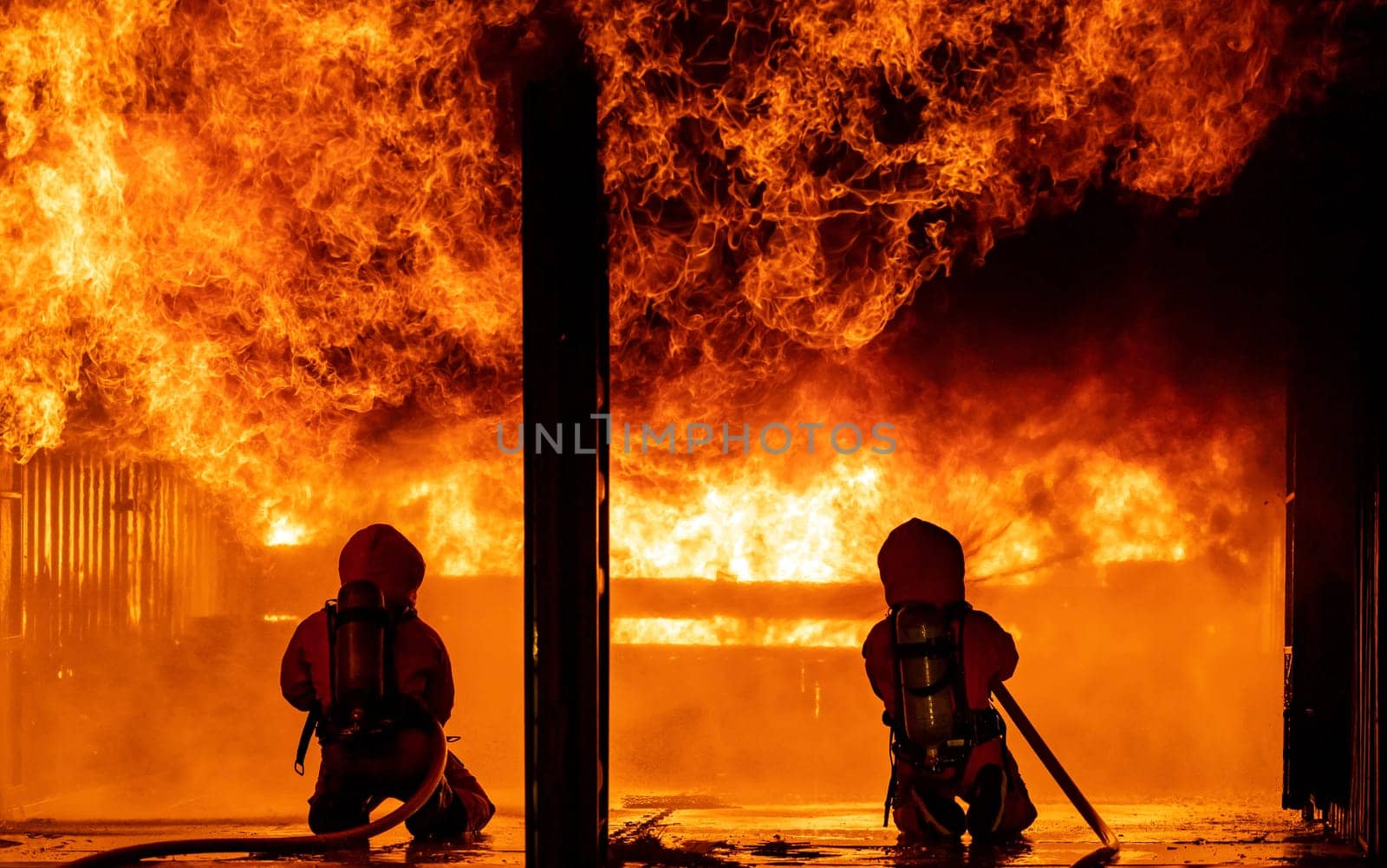 Firefighters using water fog fire extinguisher to fighting with the fire flame in large building. Firefighter and industrial safety disaster and public service concept.