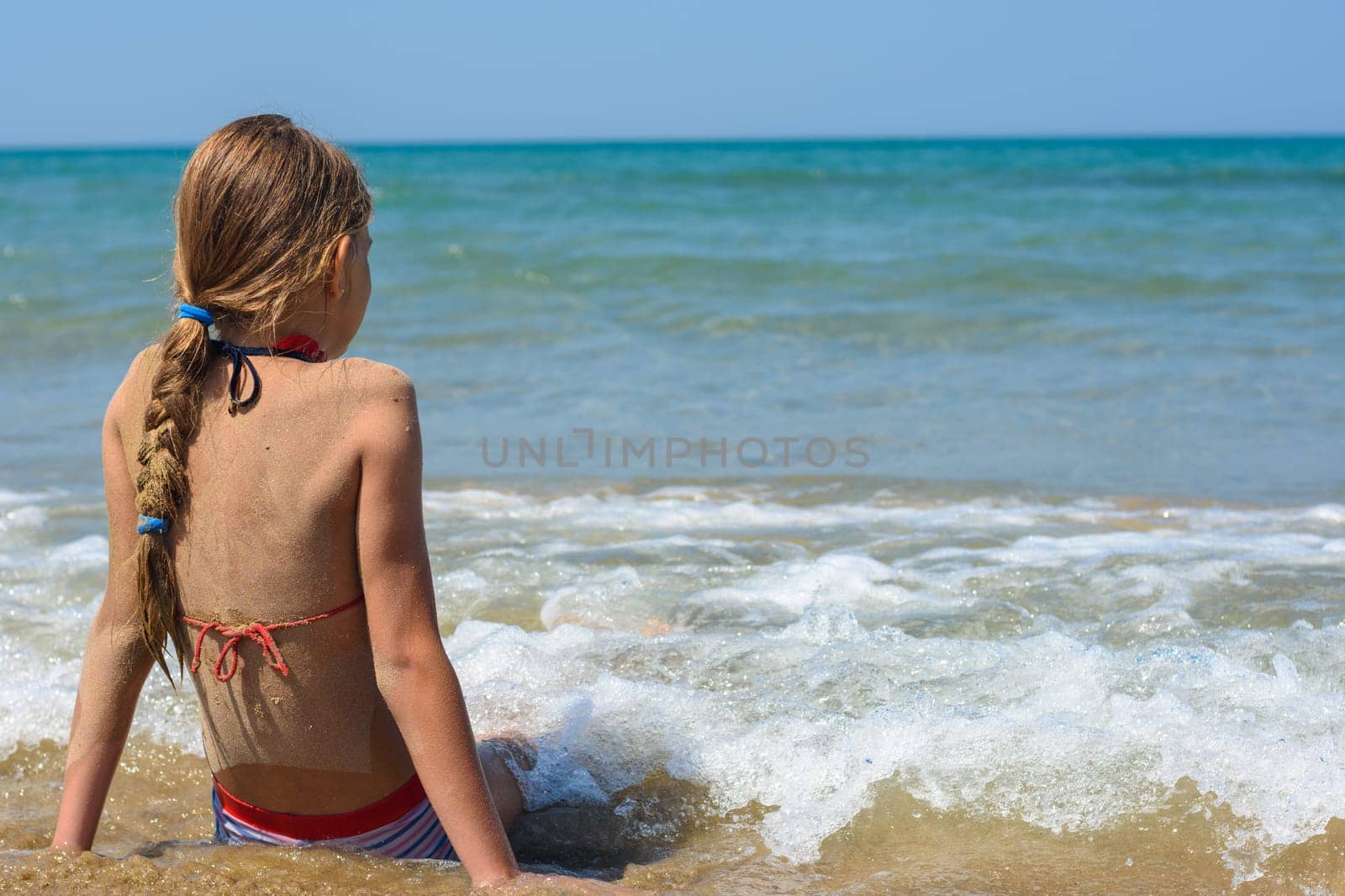 A girl sits on a sandy sea beach and looks into the distance