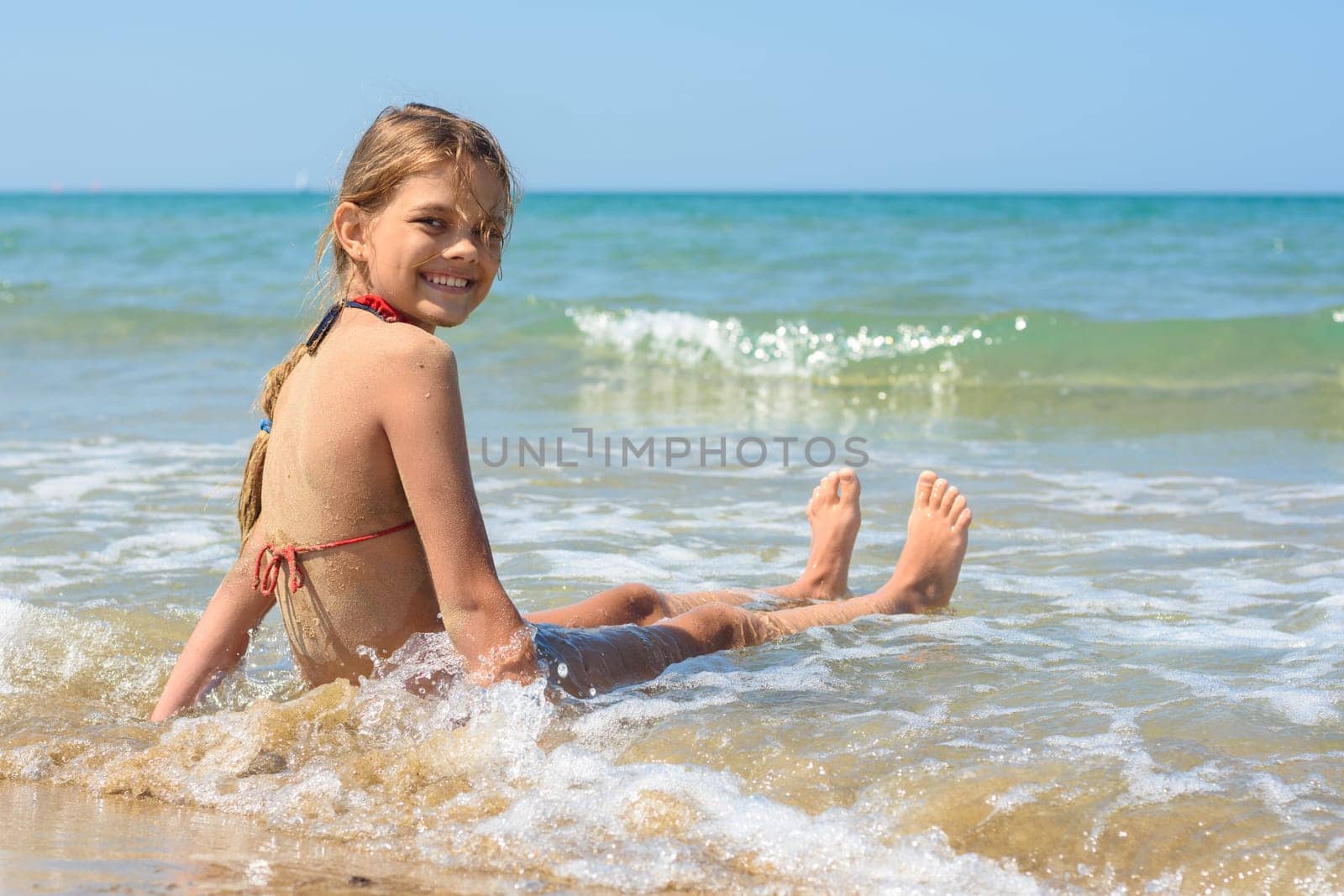 Happy girl sitting on a sandy beach and looking back smiling looked into the frame