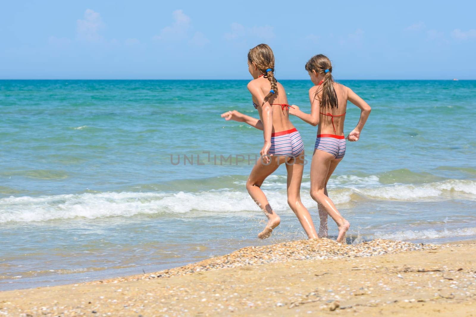 Two girls run along the shore running into the sea