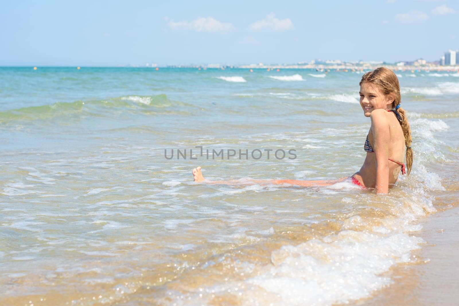 A girl of ten years old sits in the water on an empty seashore