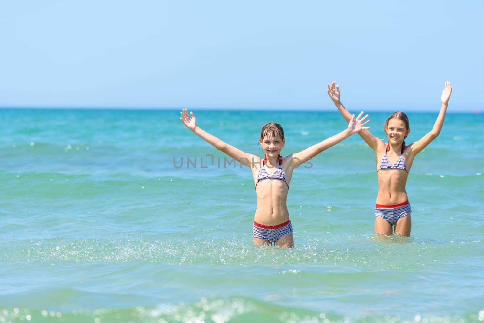 Children stand in sea water and joyfully raise their hands up