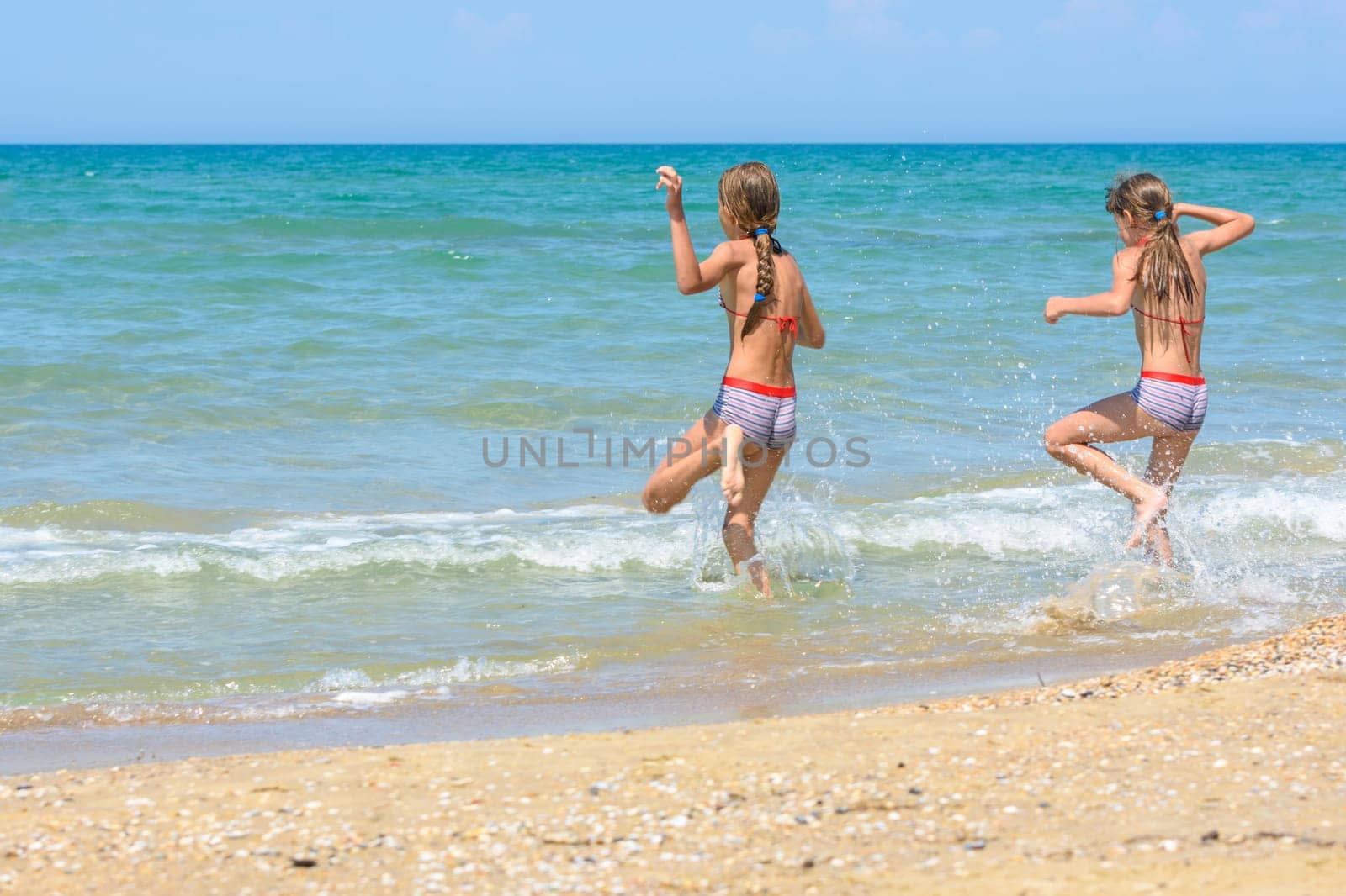 Two sisters run into the sea on a hot sunny day