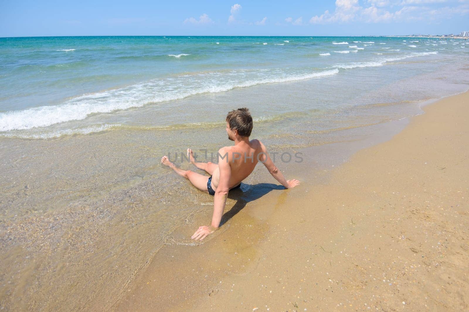 A man sits on an empty sandy sea beach in the water