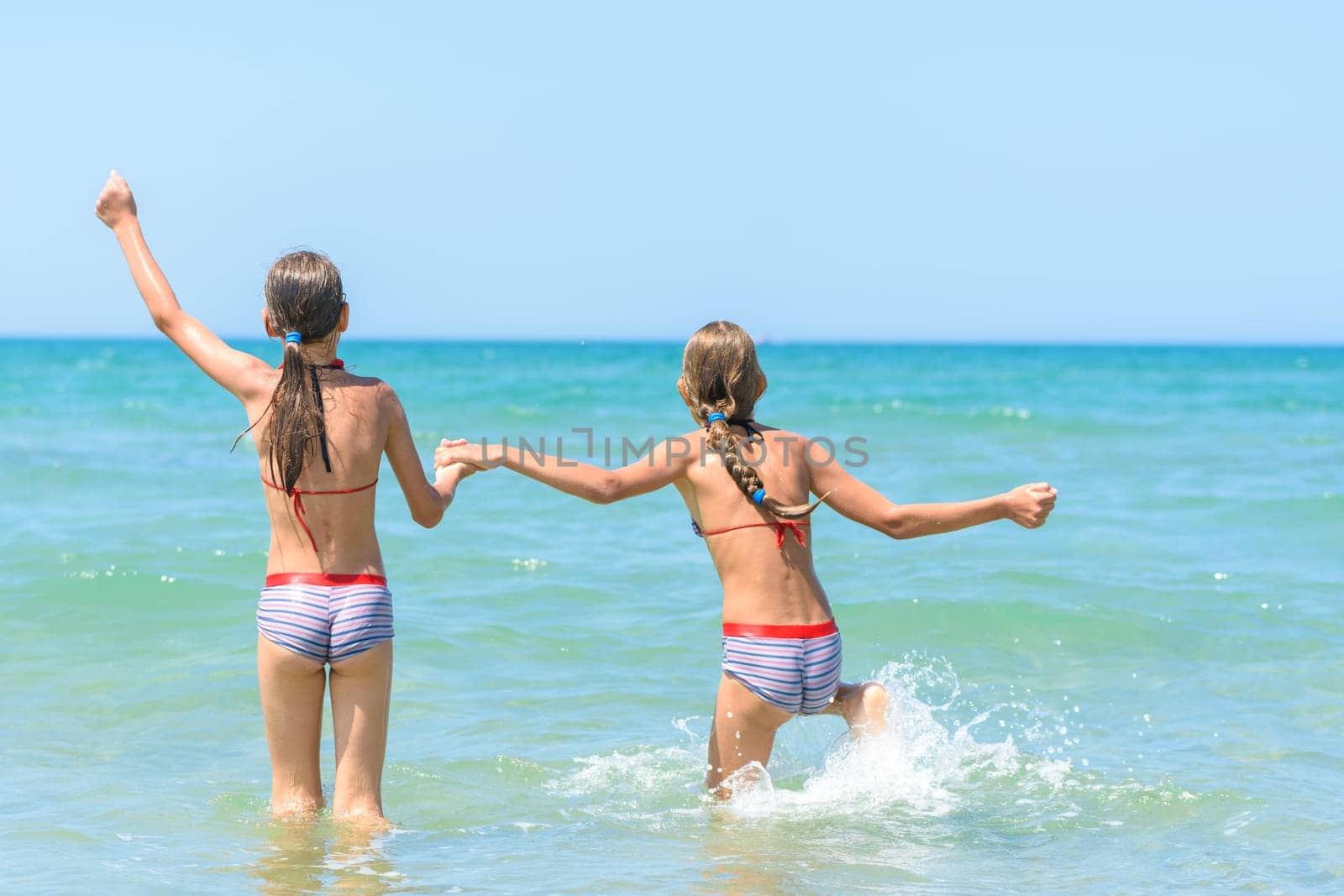 Sisters joyfully and happily run into the sea on a hot sunny day