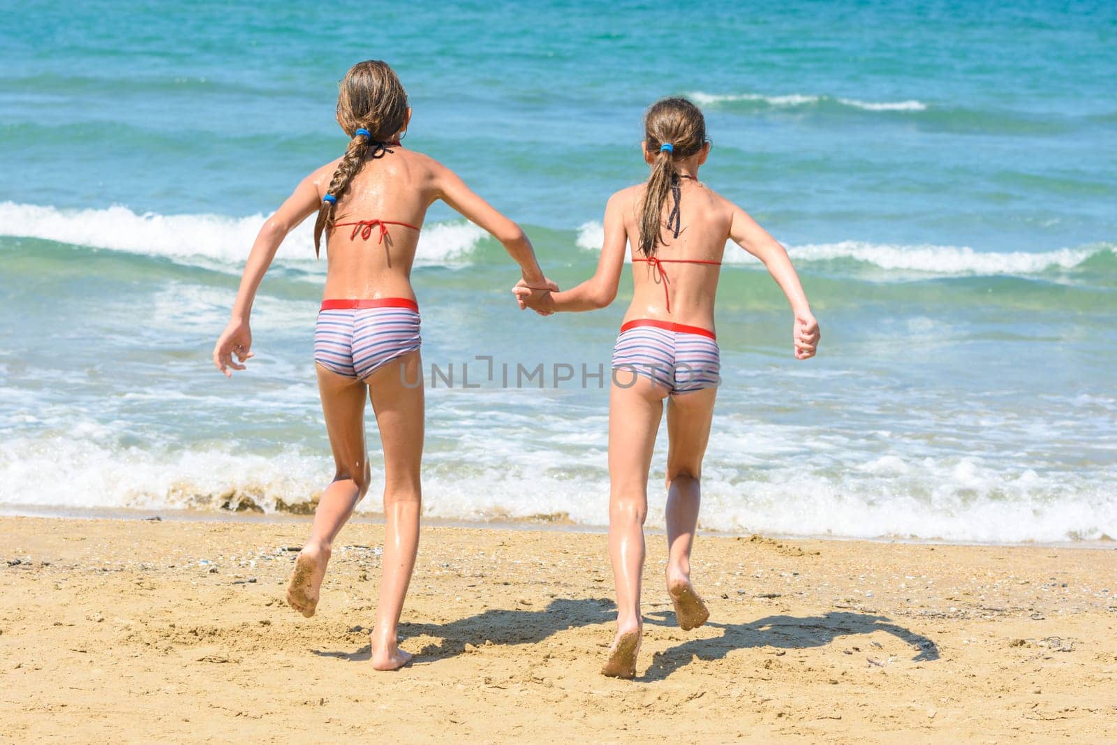 Two little sisters running to swim in the sea, back visas