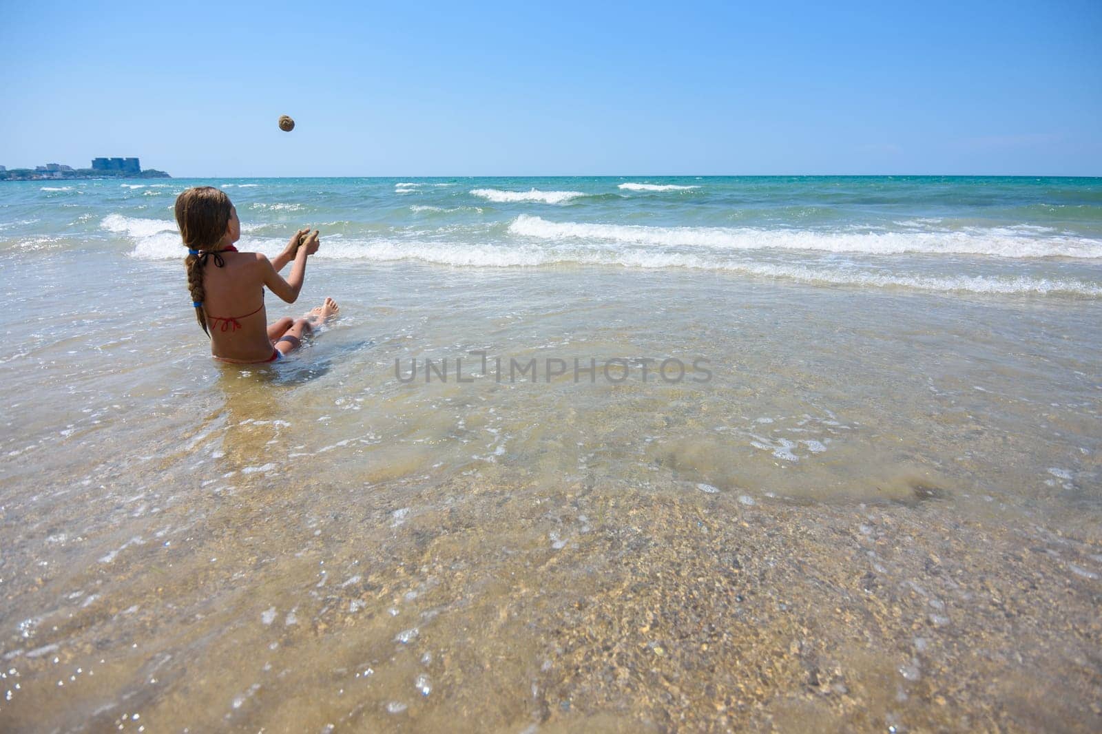 Girl sitting on the seashore and throws sand balls