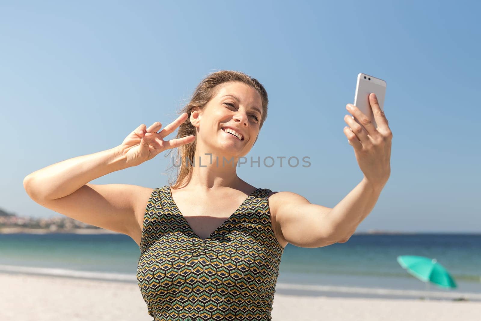 Close-up of a middle-aged blonde woman in a green dress making a selfie on the beach with the sea in the background