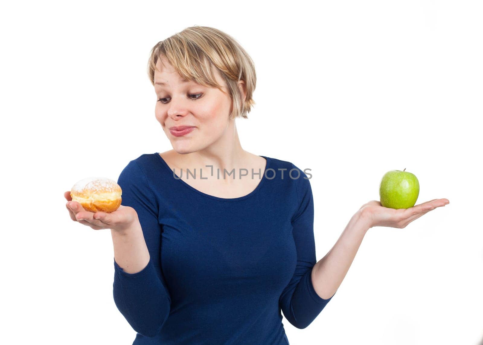 Young woman holding a donut and an apple, attracted by the donut, isolated on white
