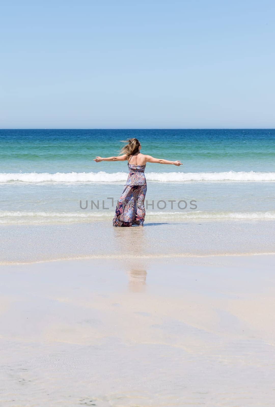 Middle-aged blonde woman relaxing at the beach with arms open enjoying her freedom facing the sea
