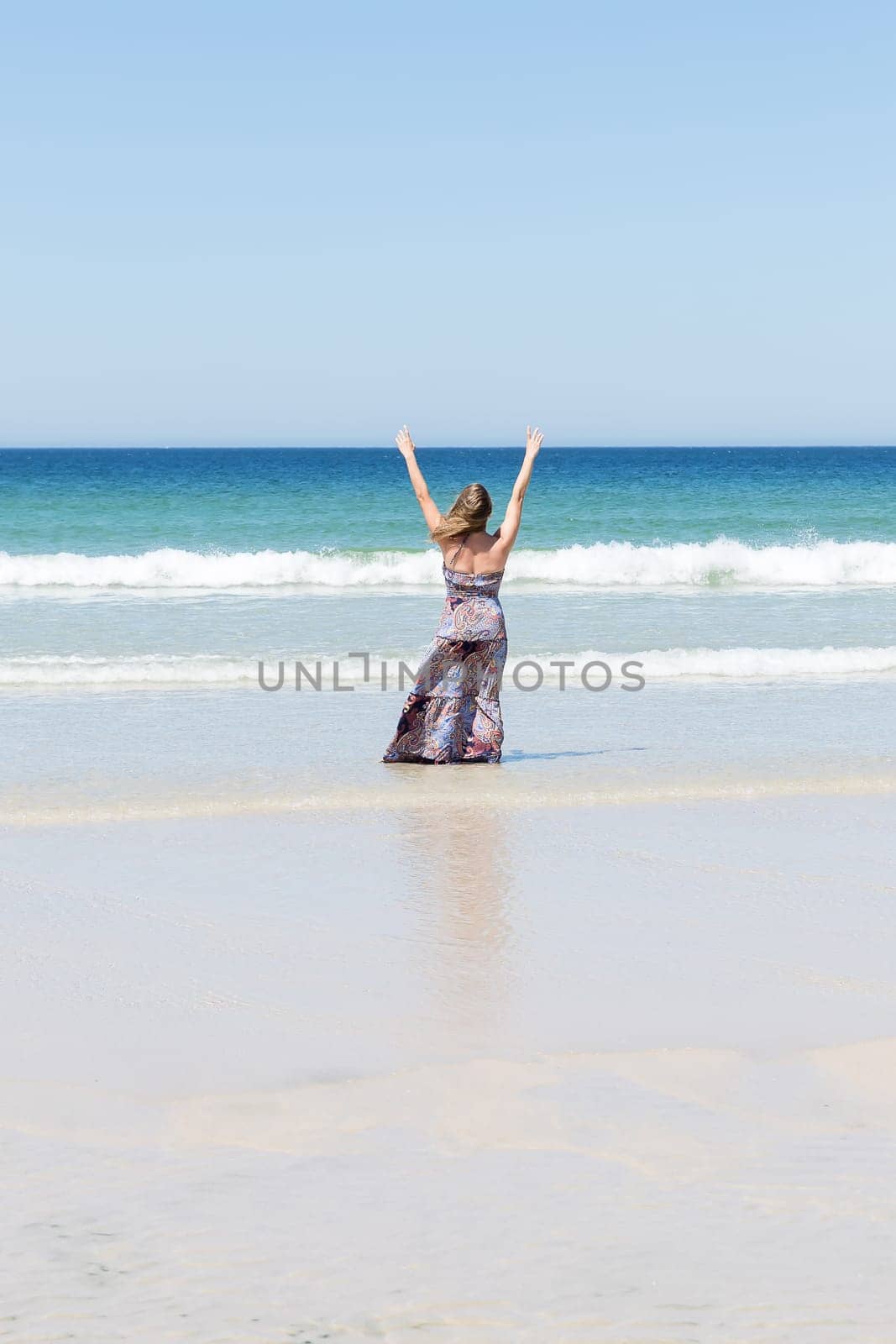 Middle-aged blonde woman relaxing at the beach with arms open enjoying her freedom facing the sea