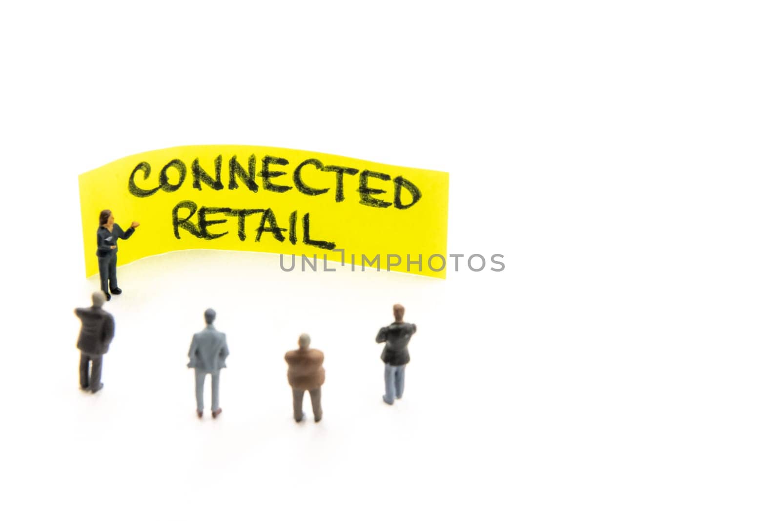 Meeting with miniature figurines posed as business people standing around post-it note with Connected Retail handwritten message in background, minimalist abstract concept with focus on text