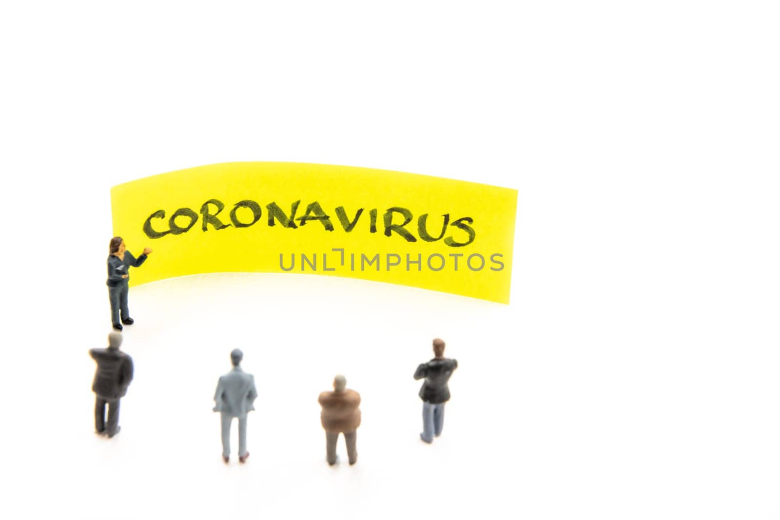 Meeting with miniature figurines posed as business people standing around post-it note with Coronavirus handwritten message in background, minimalist abstract concept with focus on text