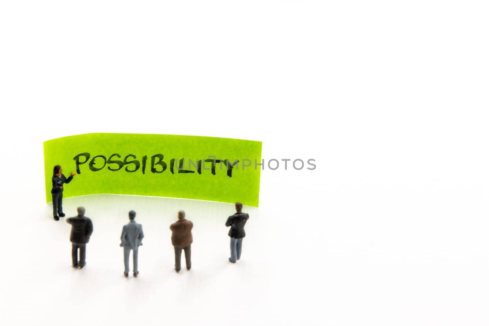 Meeting with miniature figurines posed as business people standing around post-it note with Possibility handwritten message in background, minimalist abstract concept with focus on text
