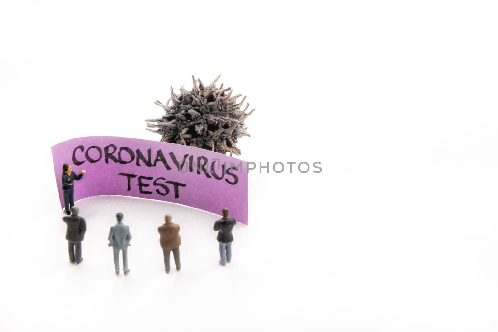 Meeting with miniature figurines posed as business people standing around post-it note with Coronavirus Test handwritten message in background, minimalist abstract concept with focus on text