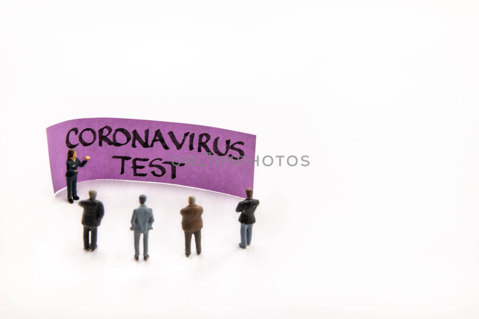 Meeting with miniature figurines posed as business people standing around post-it note with Coronavirus Test handwritten message in background, minimalist abstract concept with focus on text