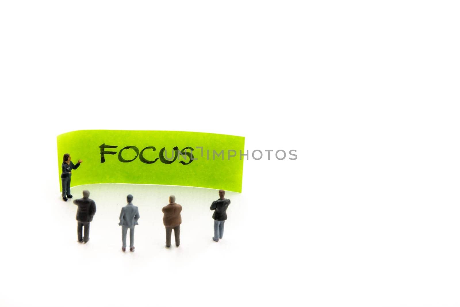 Meeting with miniature figurines posed as business people standing around post-it note with Focus handwritten message in background, minimalist abstract concept with focus on text