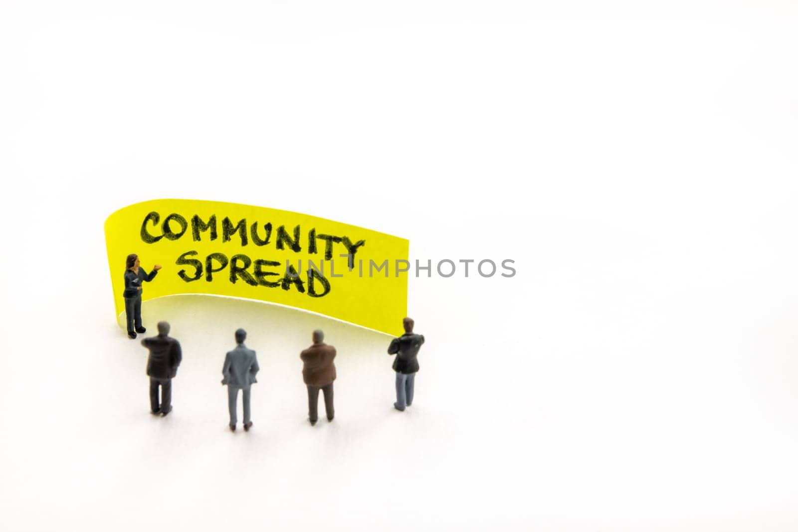 Meeting with miniature figurines posed as business people standing around post-it note with Community Spread handwritten message in background, minimalist abstract concept with focus on text