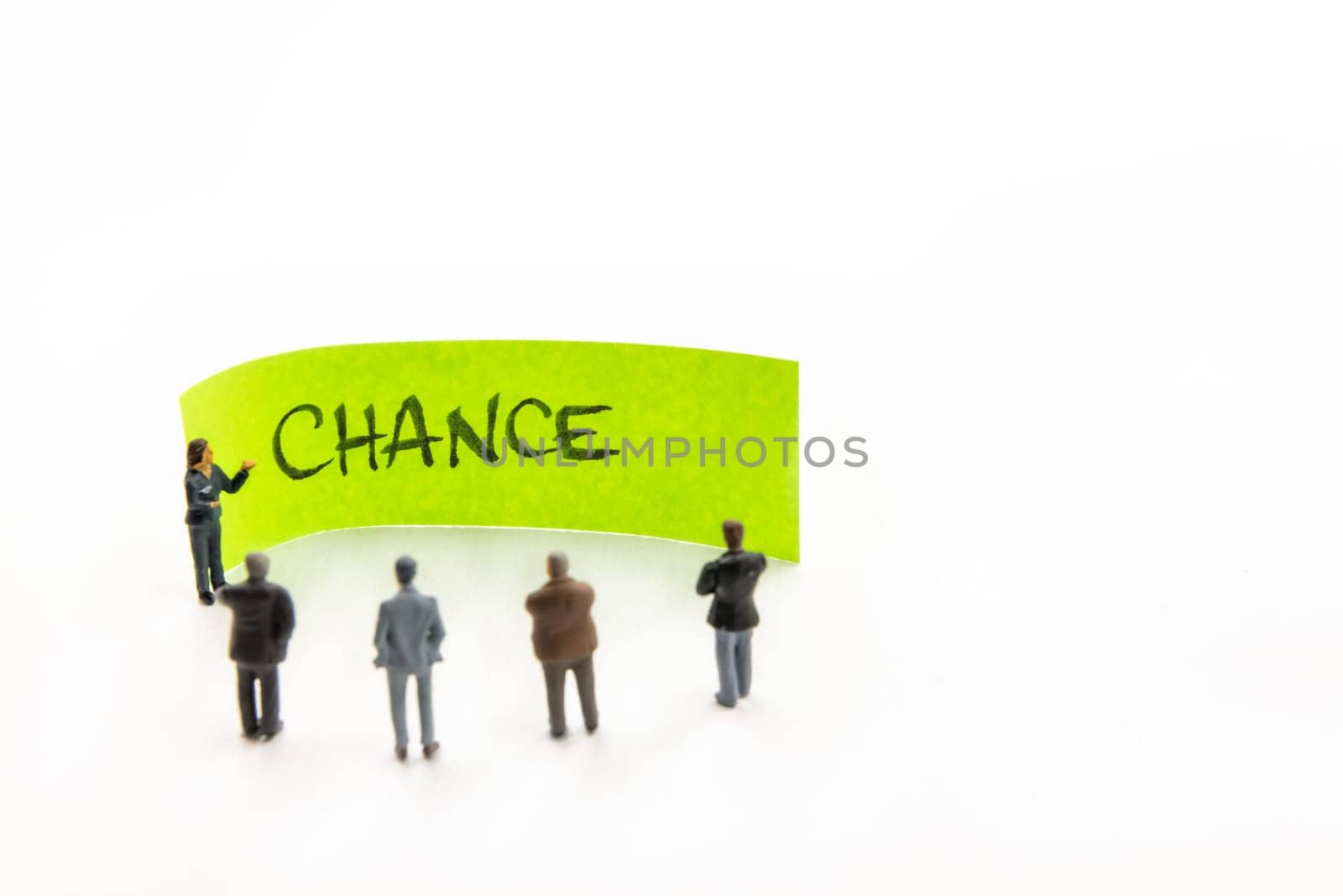Meeting with miniature figurines posed as business people standing around post-it note with Chance handwritten message in background, minimalist abstract concept with focus on text