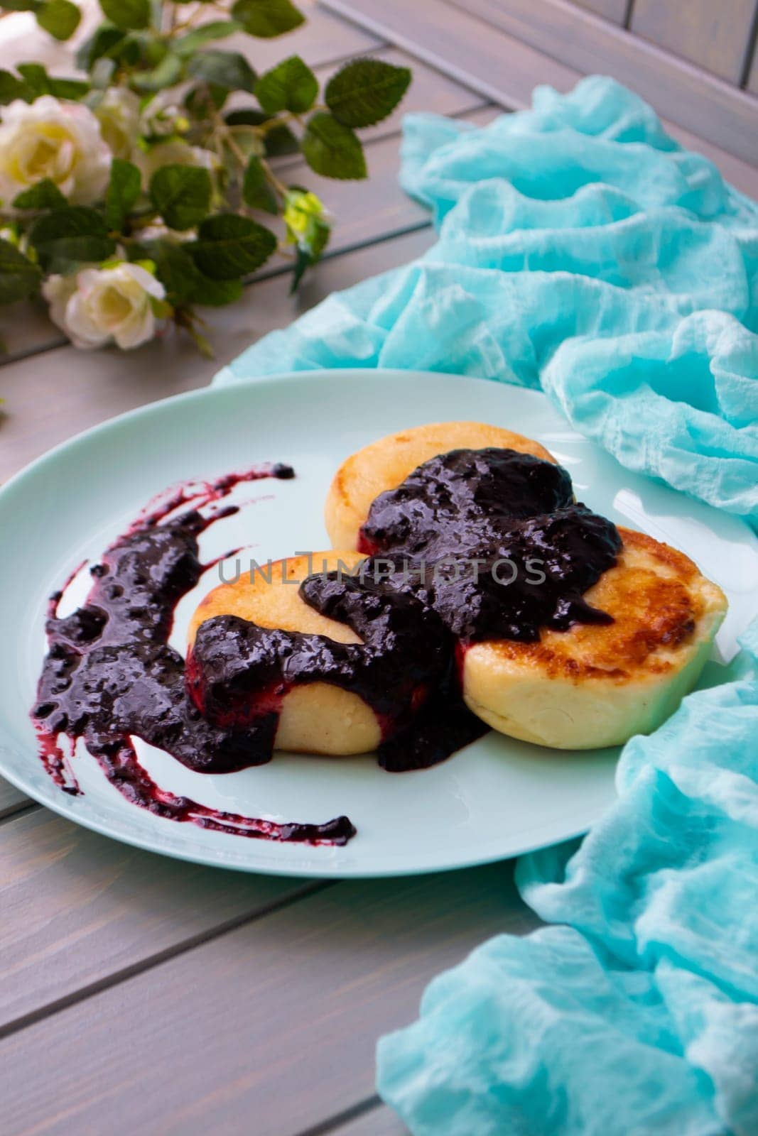 Cottage cheese pancakes with currant and blubbery jam on vintage teal plate, vertical image