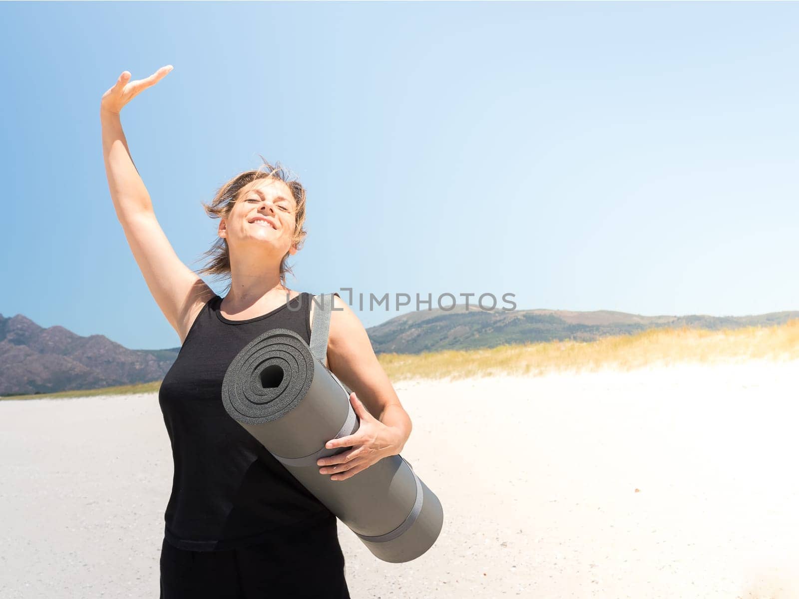 Woman in sportswear enjoying at the beach with a rolled-up mat under her arm . Copy space.