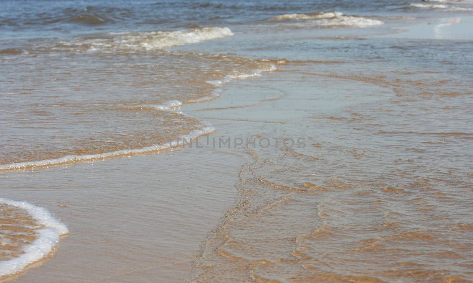 Waves with whitecaps flood the sandy beach.