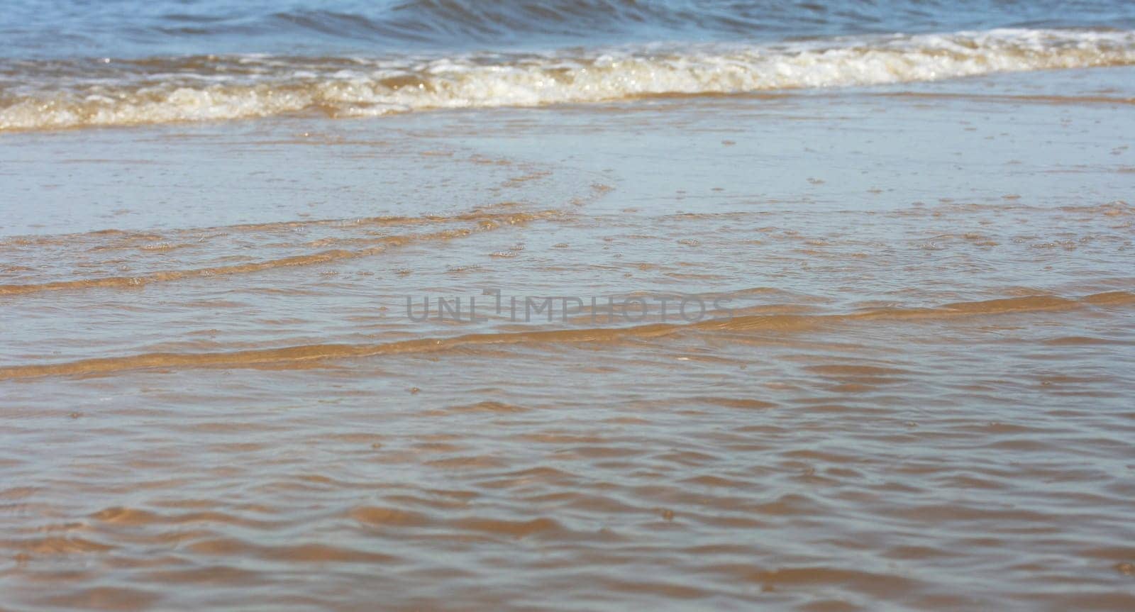 Waves with whitecaps flood the sandy beach.