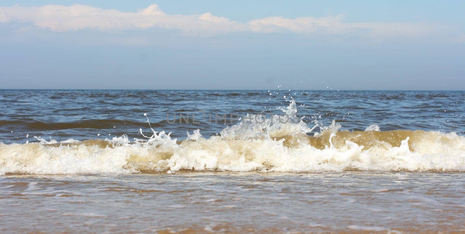 Waves with whitecaps flood the sandy beach.