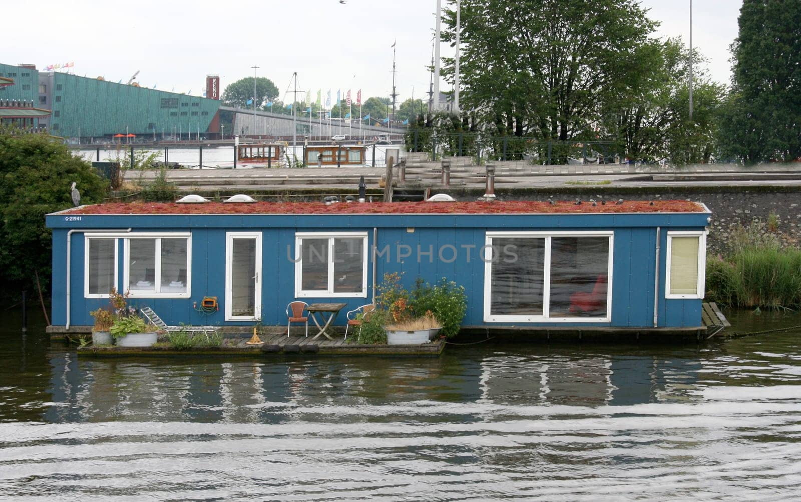 A blue house boat with white window frames and a small terrace.