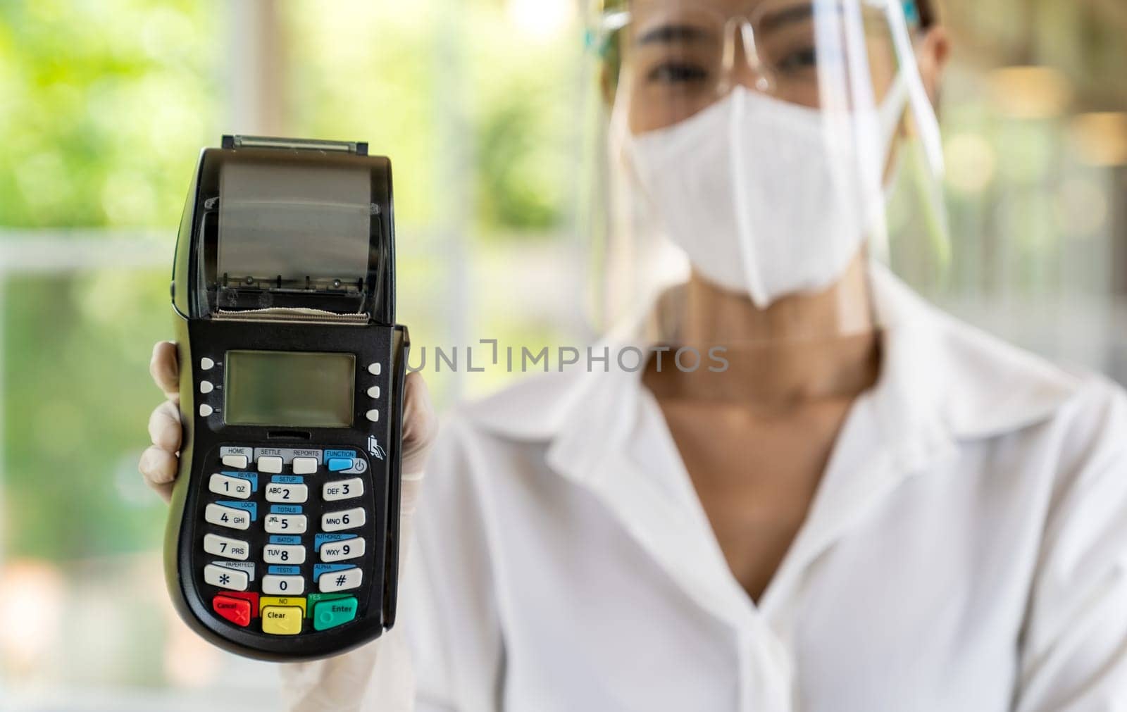 Portrait attractive asian waitress wear face mask and face shield hold credit card reader for contactless payment with indoor restaurant background. New normal restaurant contactless payment concept.