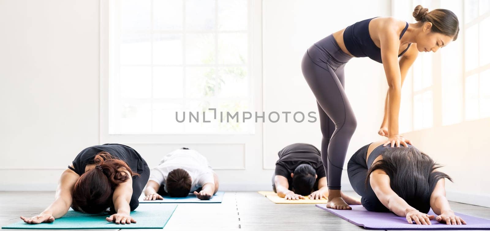 Panorama Asian sporty people learning Yoga class in fitness club. Instructor coaching and adjust correct pose on child pose to student. Yoga Practice Work out fitness healthy lifestyle concept.