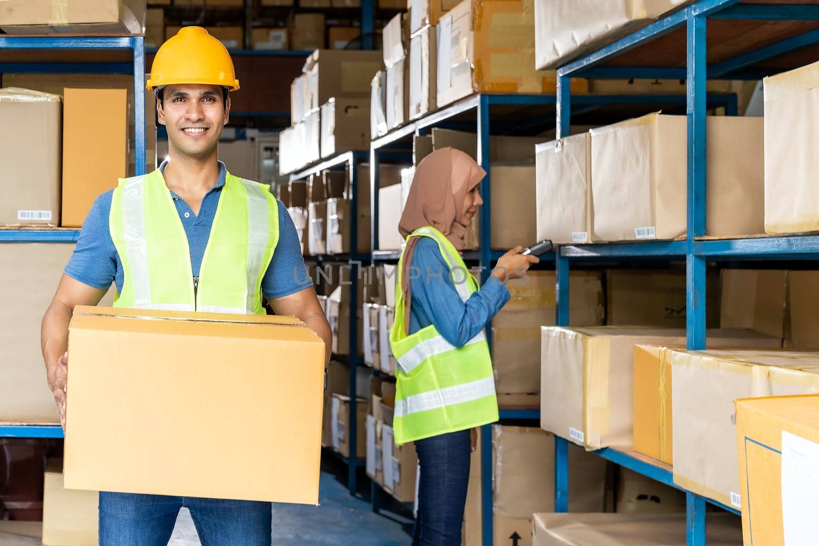 Portrait of Indian warehouse worker hold cardboard box packaging with muslim asian worker do inventory in warehouse distribution center environment. Using in business warehouse and logistic concept.
