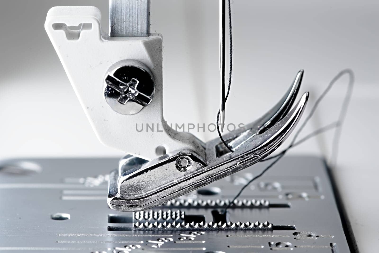 4 - Super macro image with selective focus on the needle and thread. Shows mechanism and working area of a white and metal sewing machine.