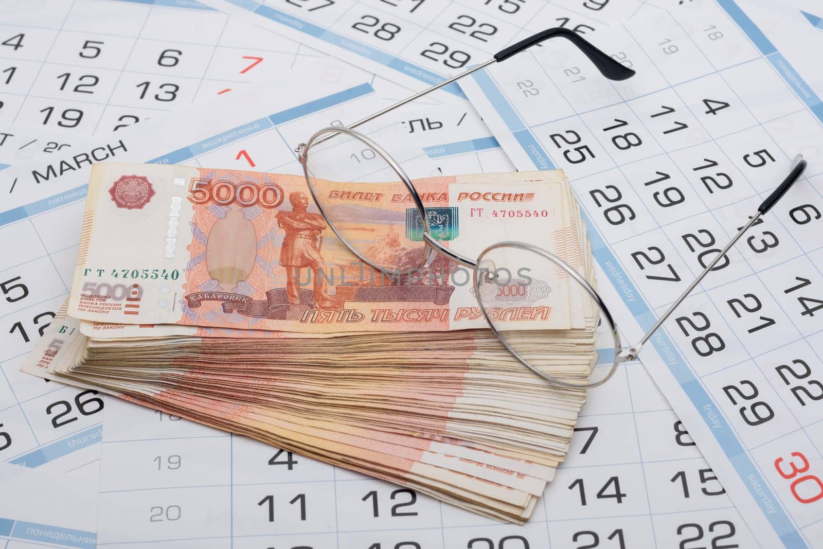 Glasses lie on a bundle of five-thousandth Russian banknotes, background from calendar sheets