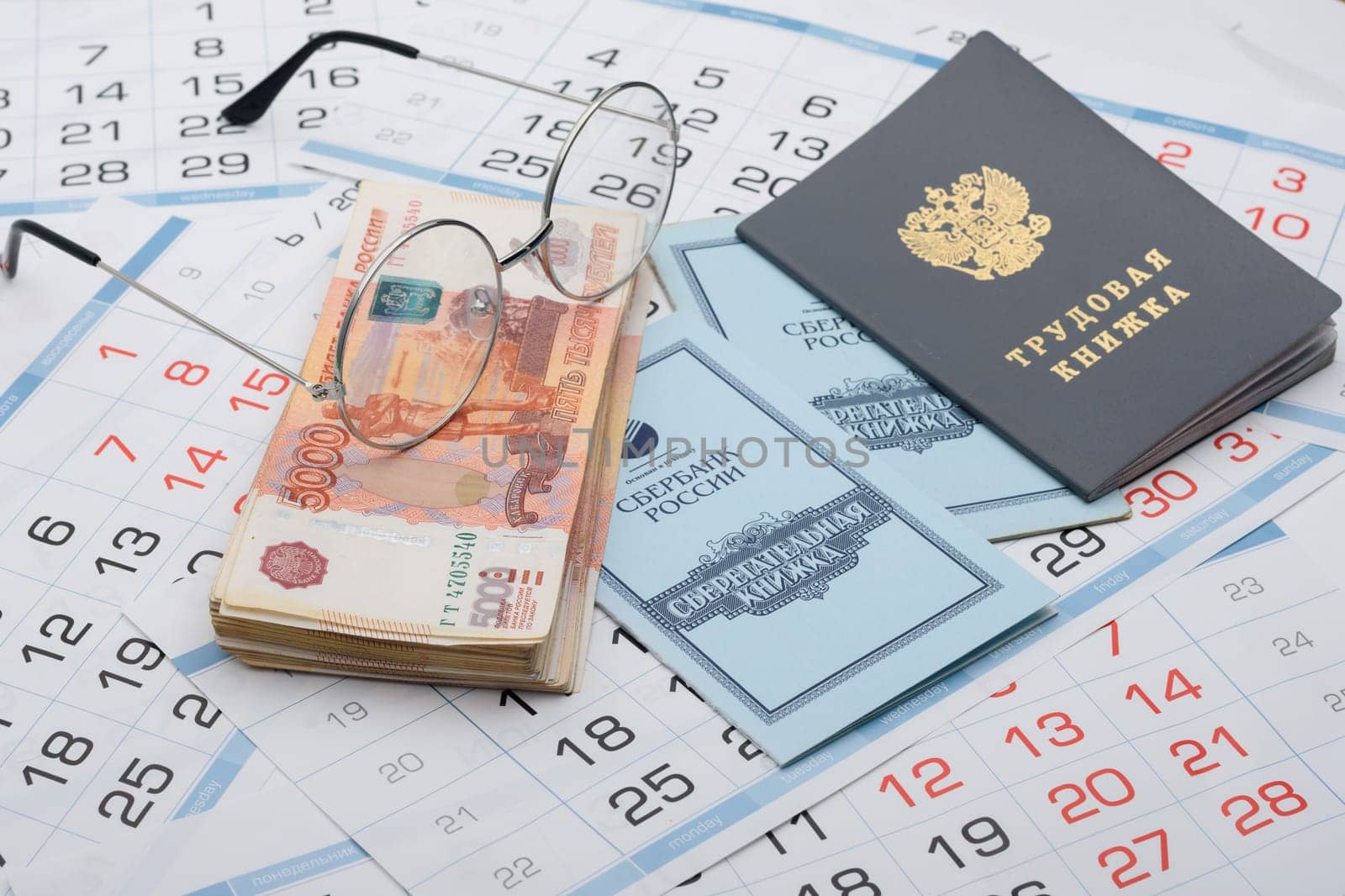Anapa, Russia - 29.06.2020: On the background of the calendars lie a work book, a savings book, a bundle of money and glasses