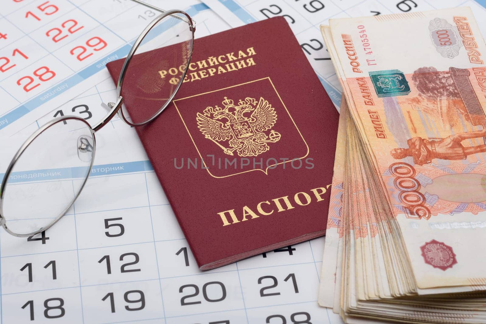 The passport of the Russian Federation lies on the background of calendar numbers, next to it lies a bundle of money and glasses
