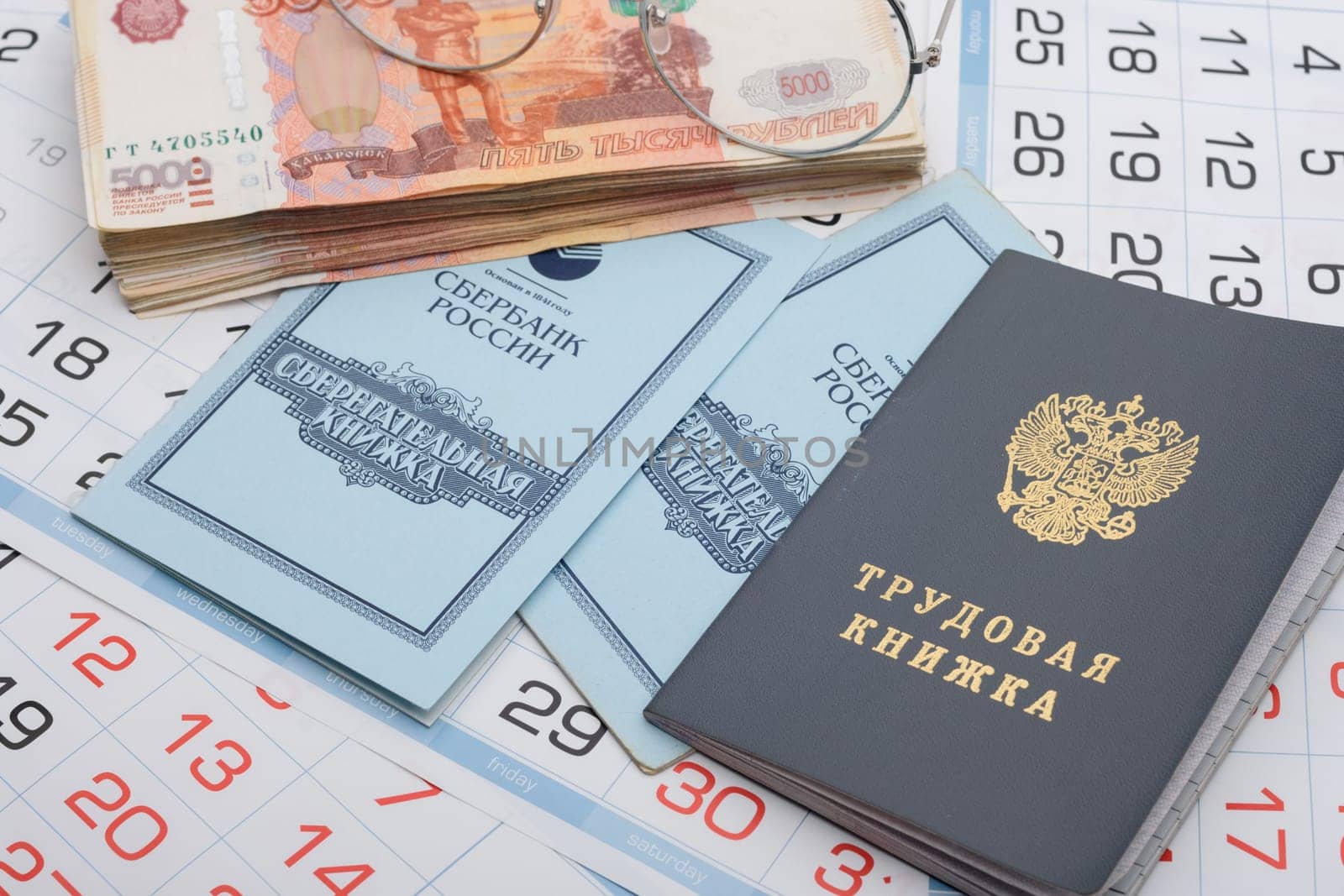 Anapa, Russia - 29.06.2020: On the background of the calendars lie a work book, a savings book, a bundle of money and glasses