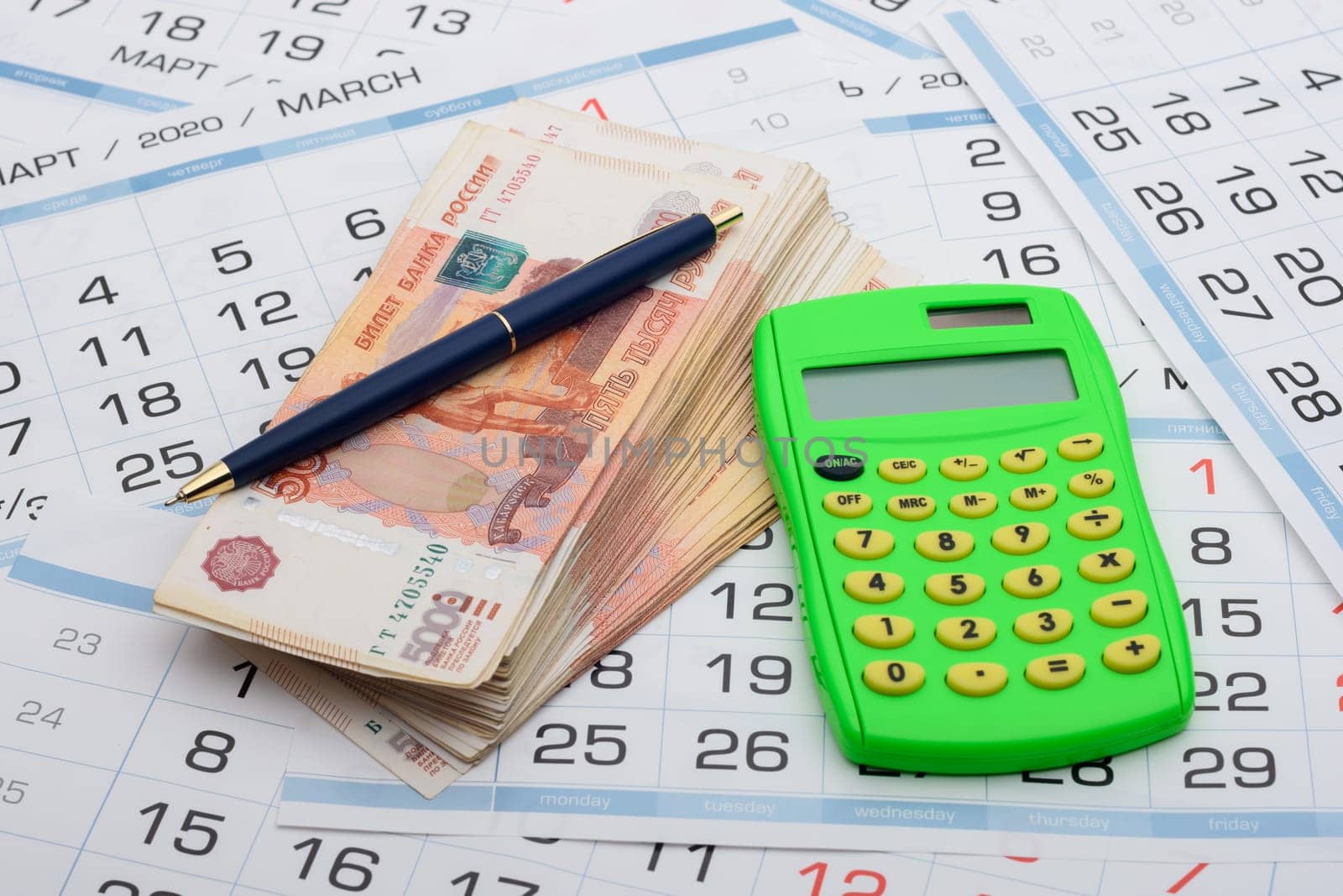 There is a wad of money on the calendar, a calculator and a pen