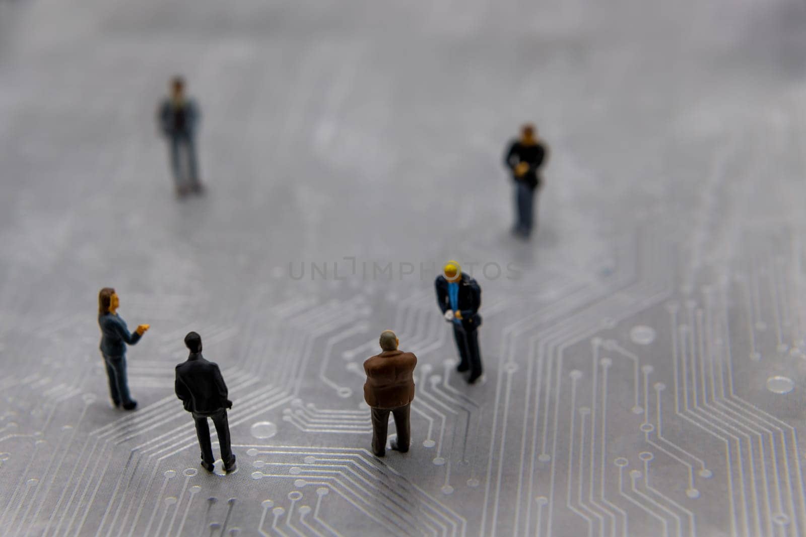 Miniature figurines posed as business people in a meeting over abstract futuristic circuit board, future business concept