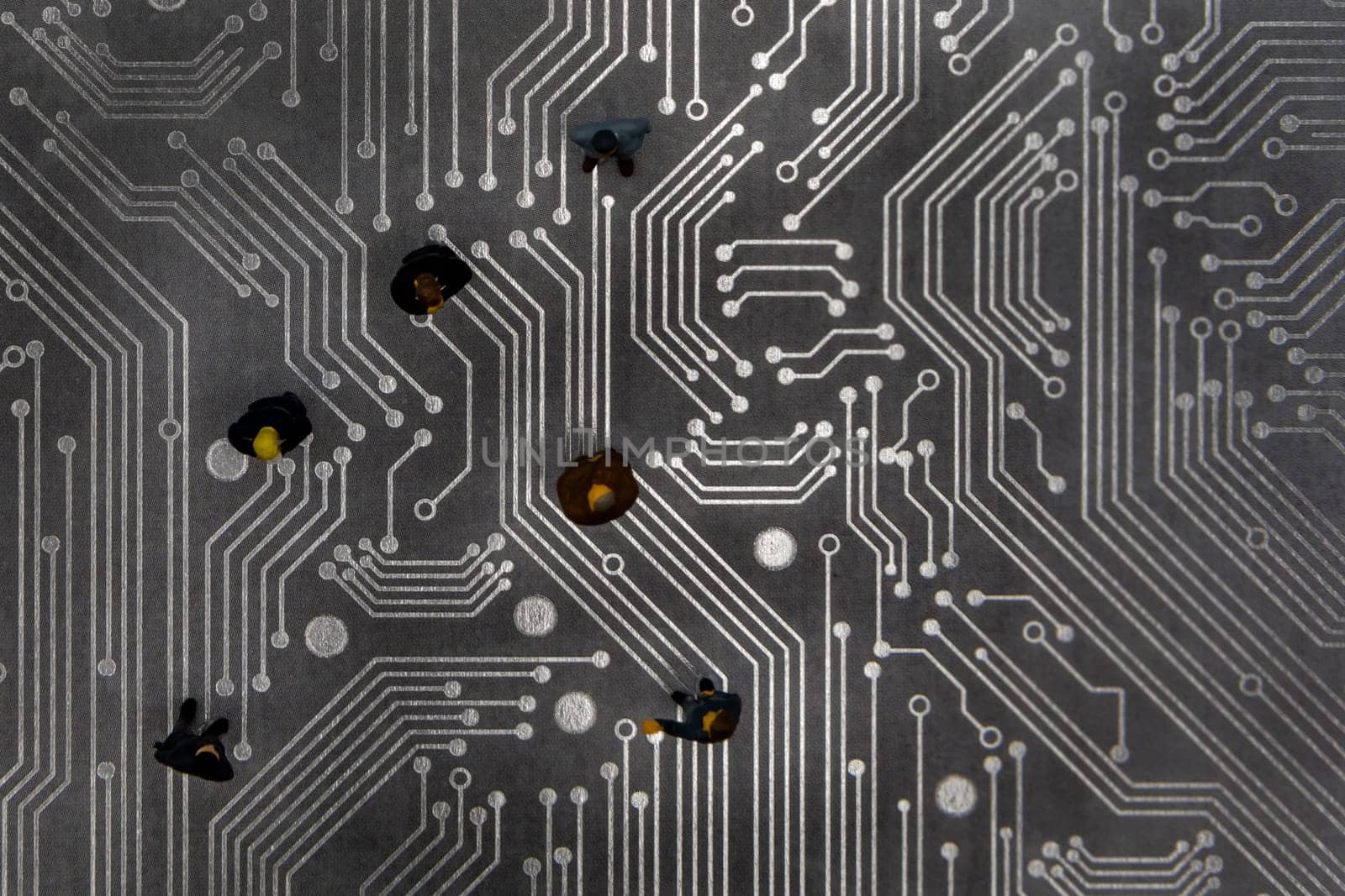 Miniature figurines posed as business people in a meeting over abstract futuristic circuit board, future business concept