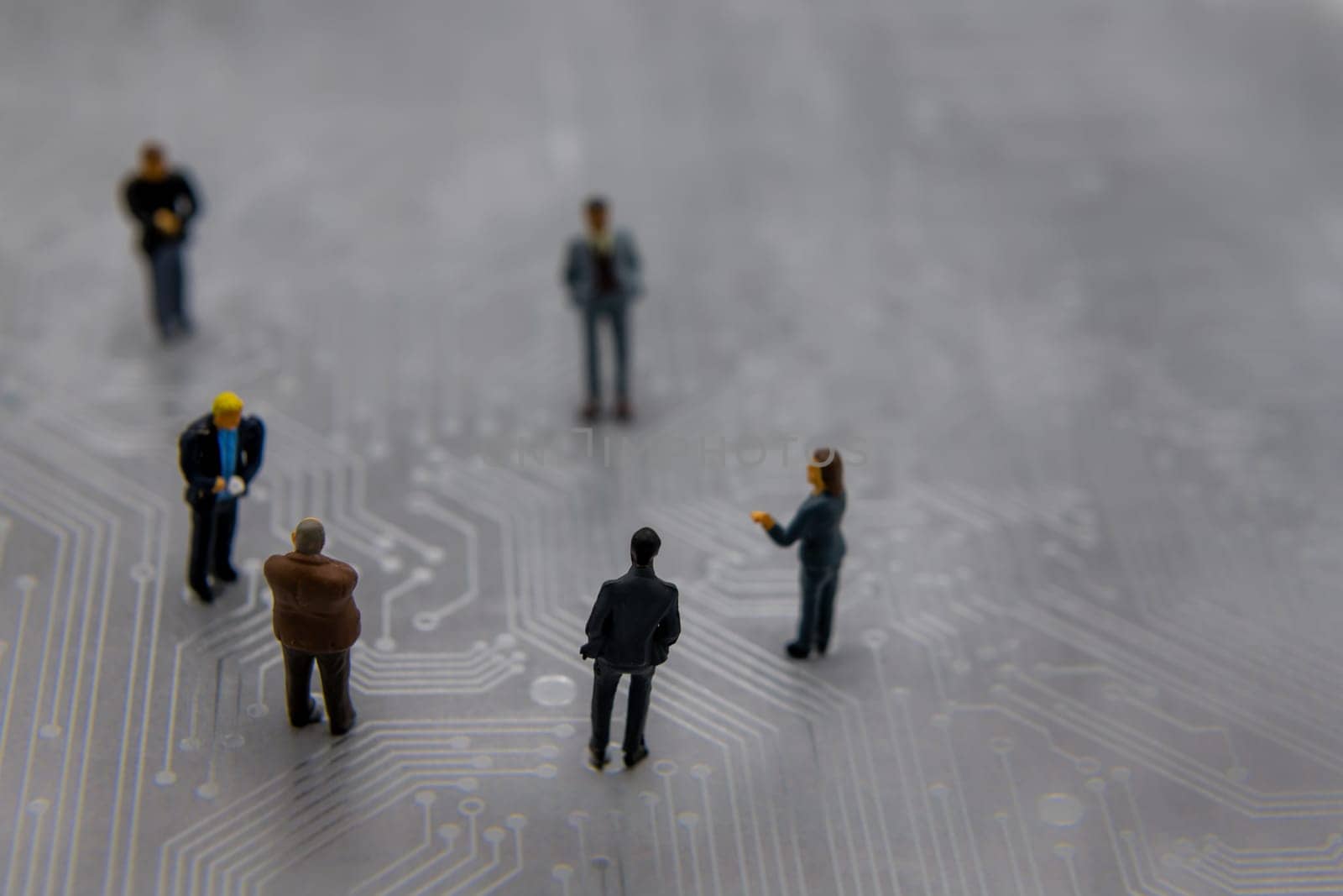 Miniature figurines posed as business people in a meeting over abstract futuristic circuit board, future business concept