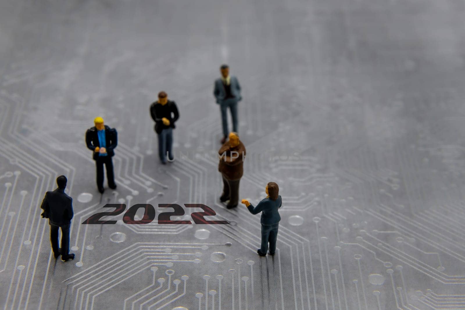 Miniature figurines posed as business people in a meeting over abstract futuristic circuit board with text year 2022