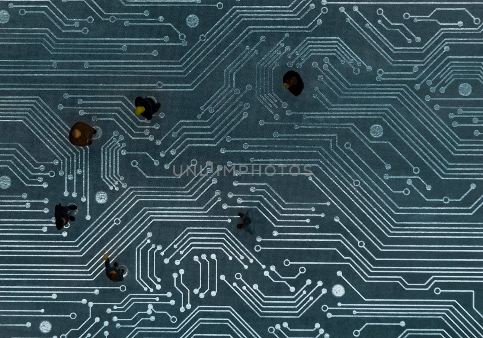 Miniature figurines posed as business people in a meeting over abstract futuristic circuit board, future business concept