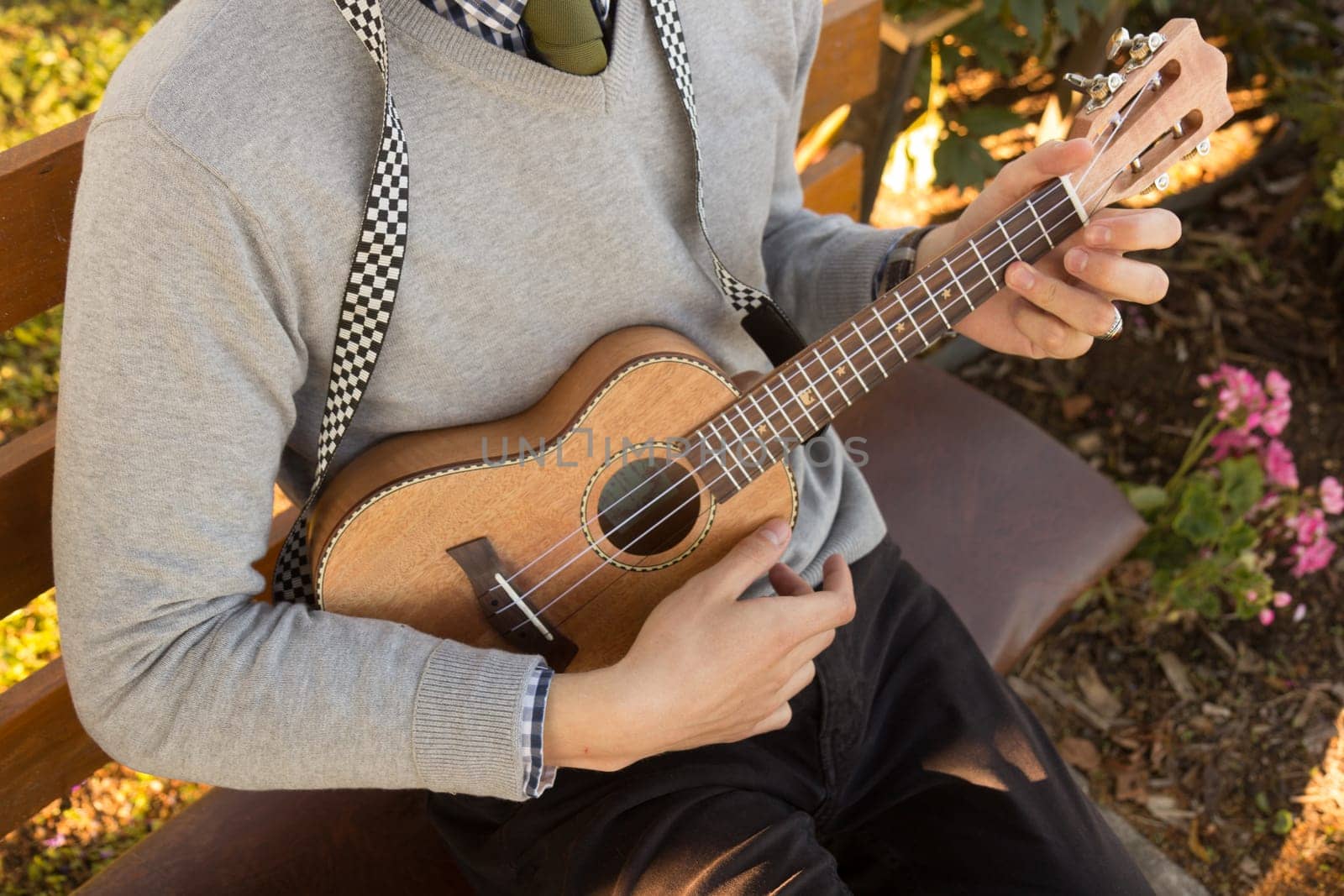 Young man sitting on bench in the park and playing ukulele.