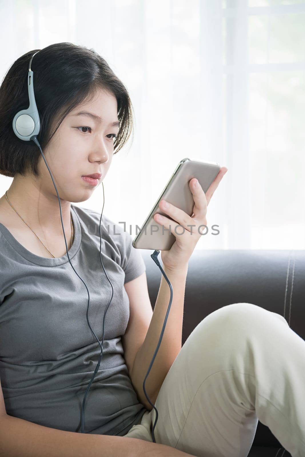 Close up young asian woman short hair listening music from mobile phone on the couch