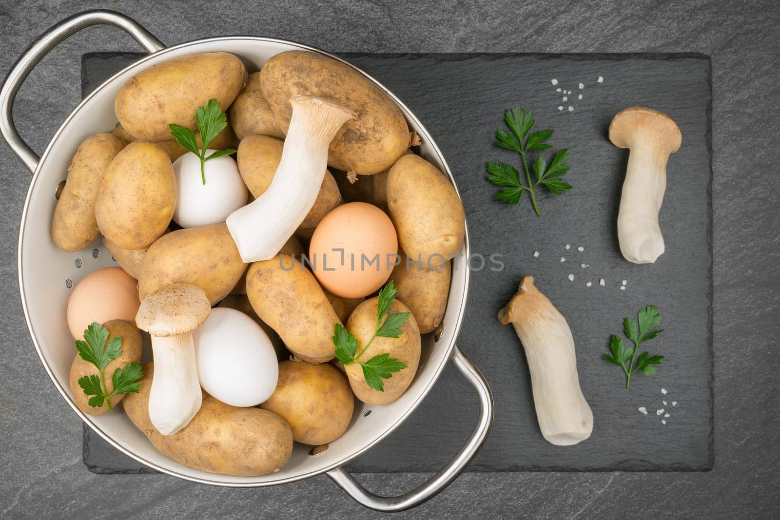 Two King Trumpet Mushrooms and a white and a brown egg on a slate slab with coarse salt grains. With copyspace. Flat lay.