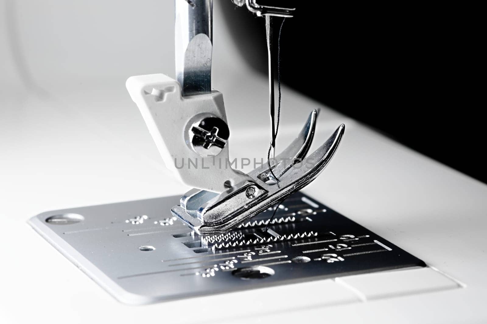 3 - Close macro sewing machine image with selective focus showing needle, thread, presser foot, feed dogs and throat plate.