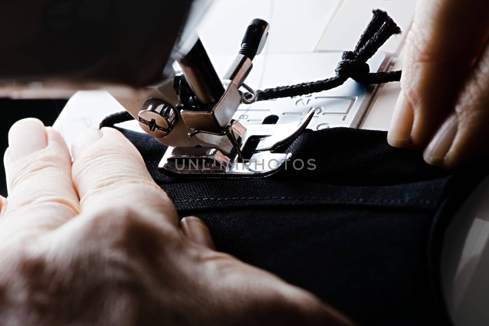 From right to left, a seam is stitched on a black homemade face covering or face mask. Guided by older weathered hands.